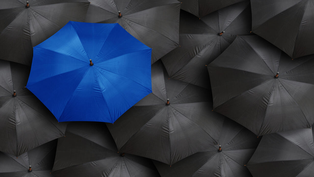 one blue umbrella surrounded by black umbrellas 