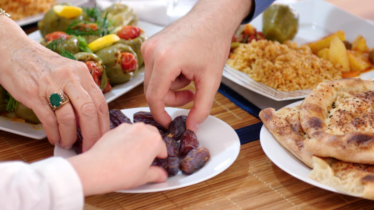 Three hands reach for a plate of dates.