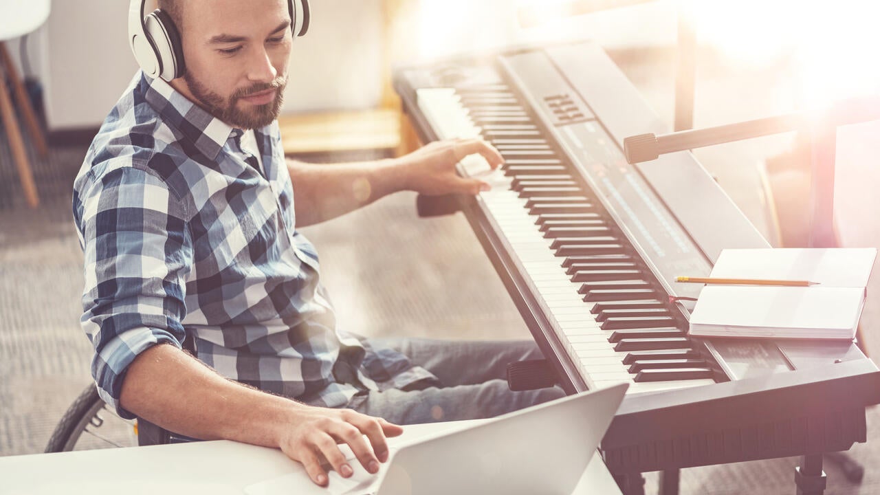 Composer sitting in semi position wearing headphones using laptop while writing new composition