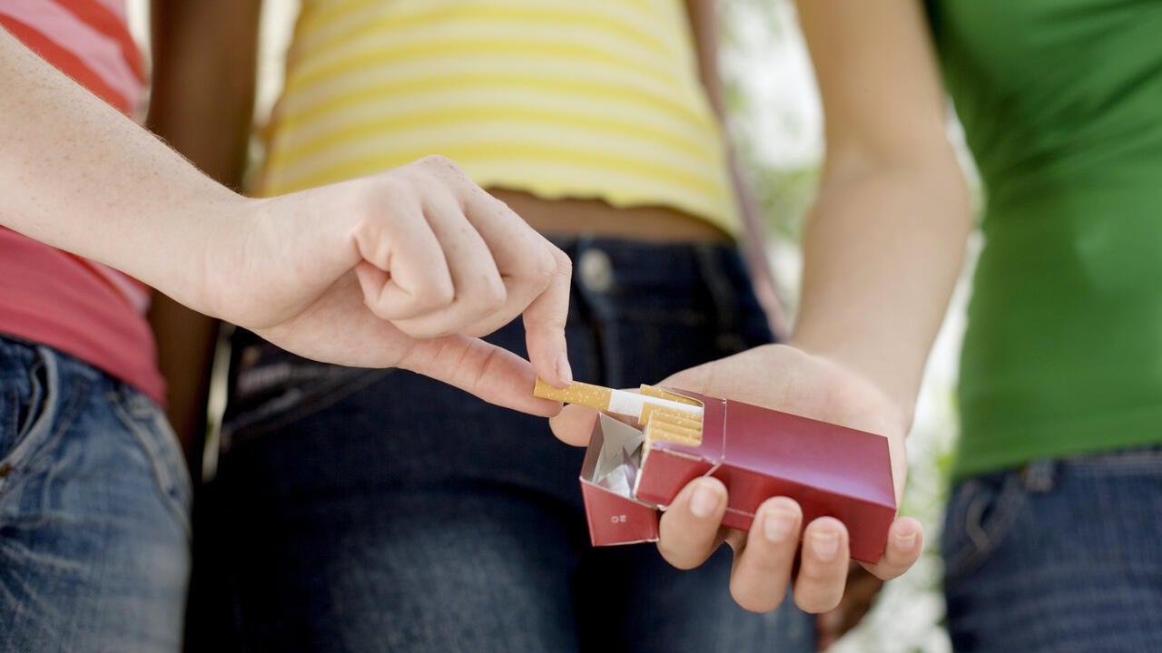 Teenage girl taking cigarette from friend cigarette pack