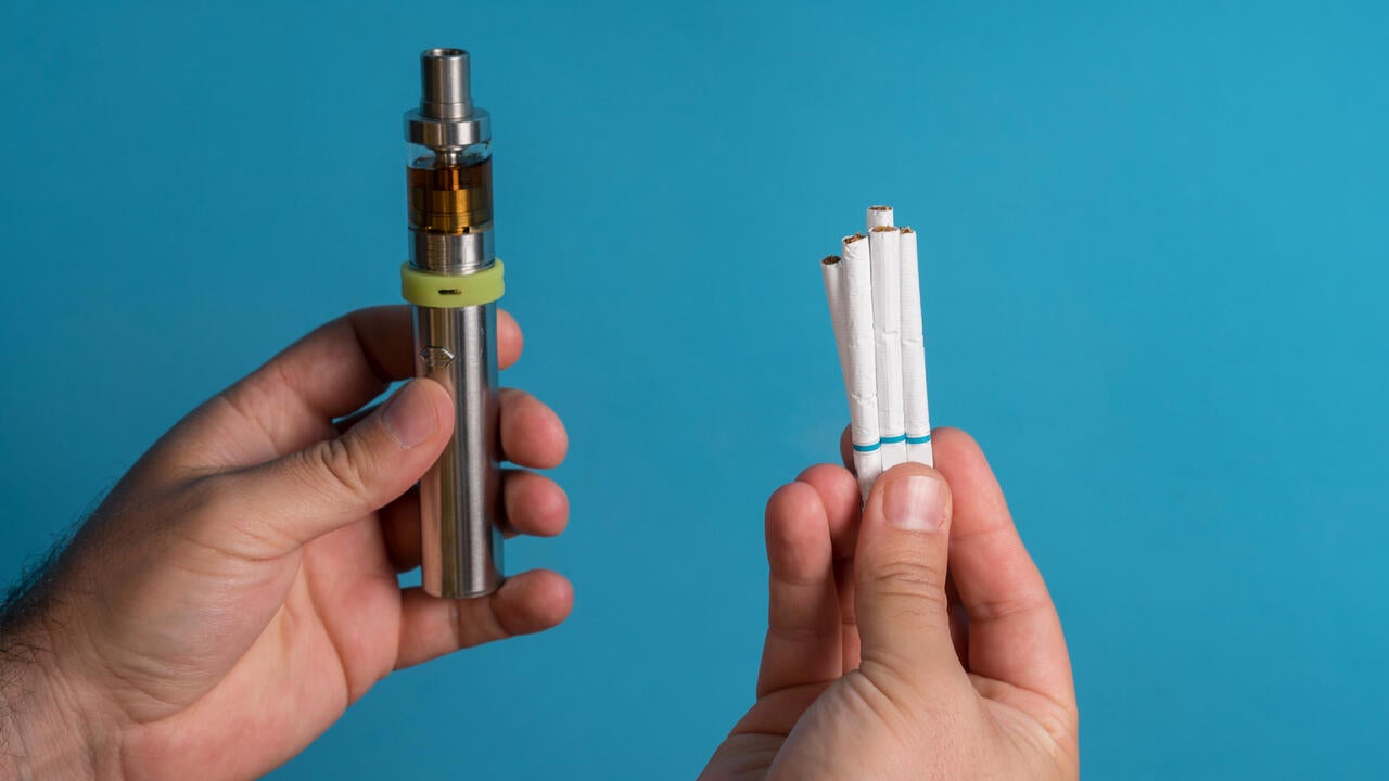 A person's hand hold e-cigarette while the other holds regular cigarettes 