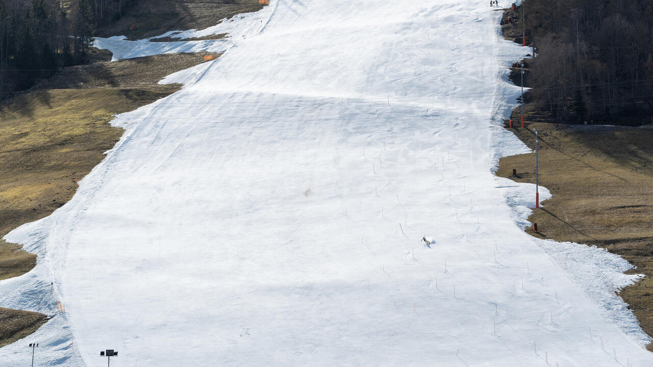 Skier slaloms on hill with snow and grass