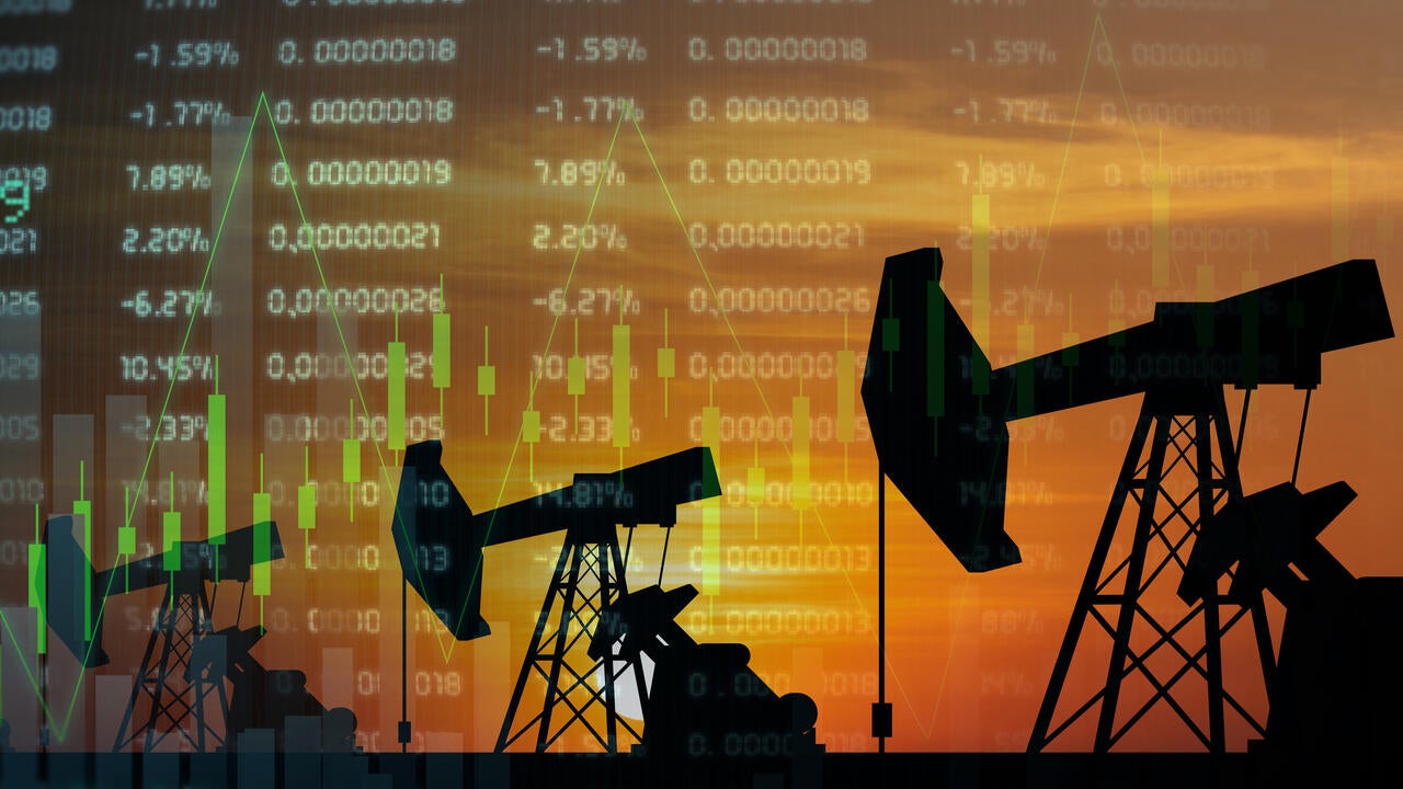 Oil derricks in silhouette with stock prices listed in the background