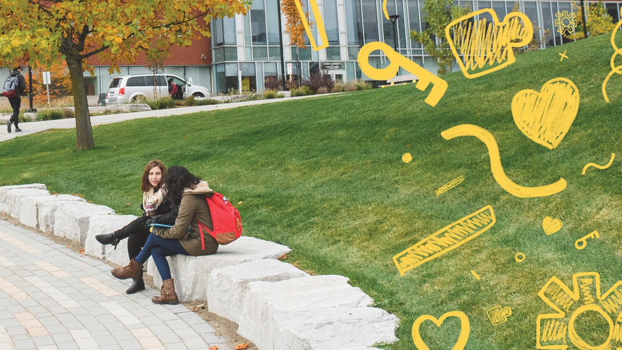 Two female students sitting on a low stone wall