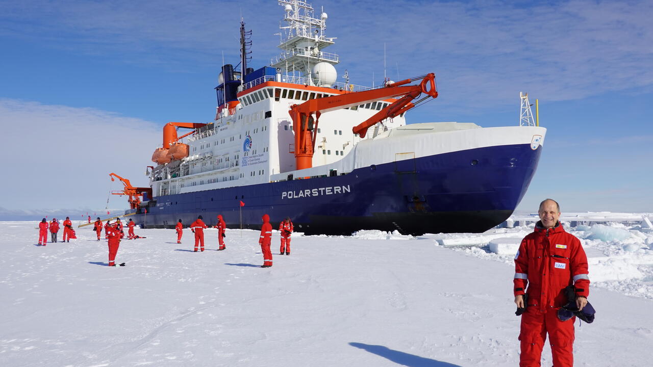Gotz Hoppe standing on Antarctic ice flow in from of ship