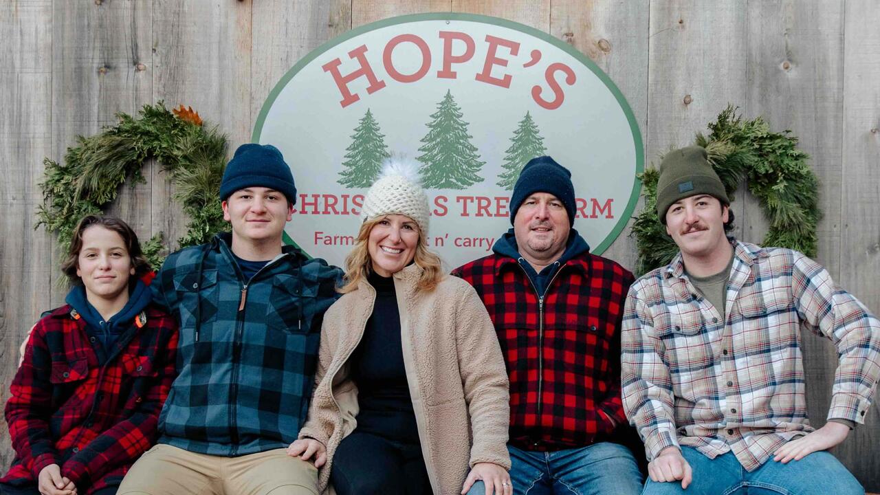 The Hope family sits together on a log with a barn behind them