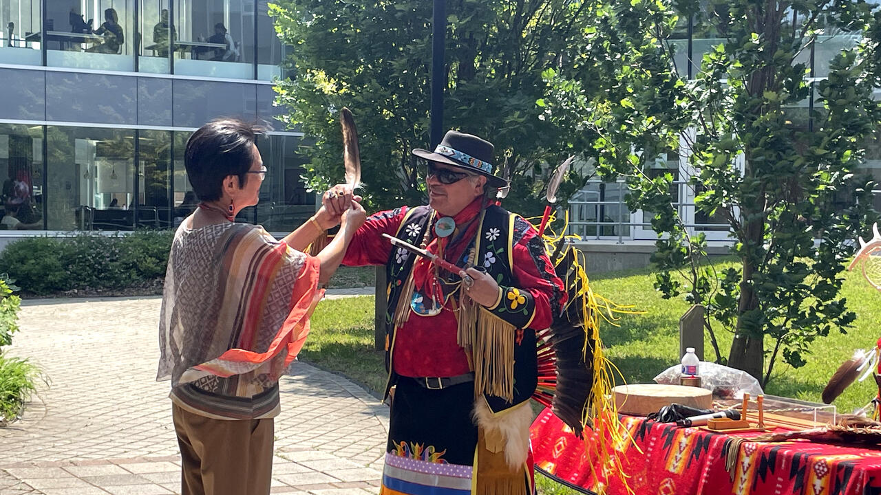 Dean Lili Liu and Elder Myeengun Henry hold up an eagle feather