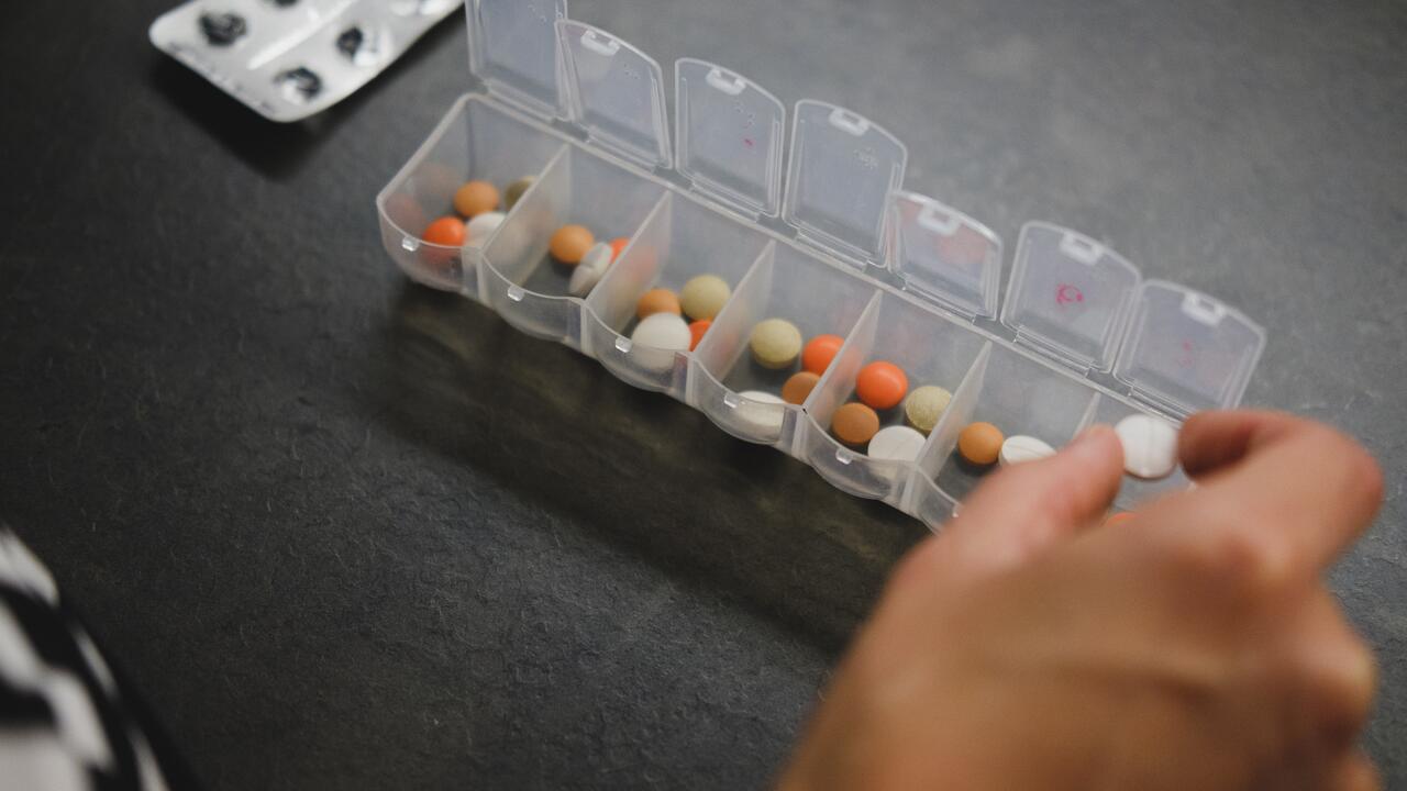 A person putting pills into a weekly organizer that already has several pills in each slot