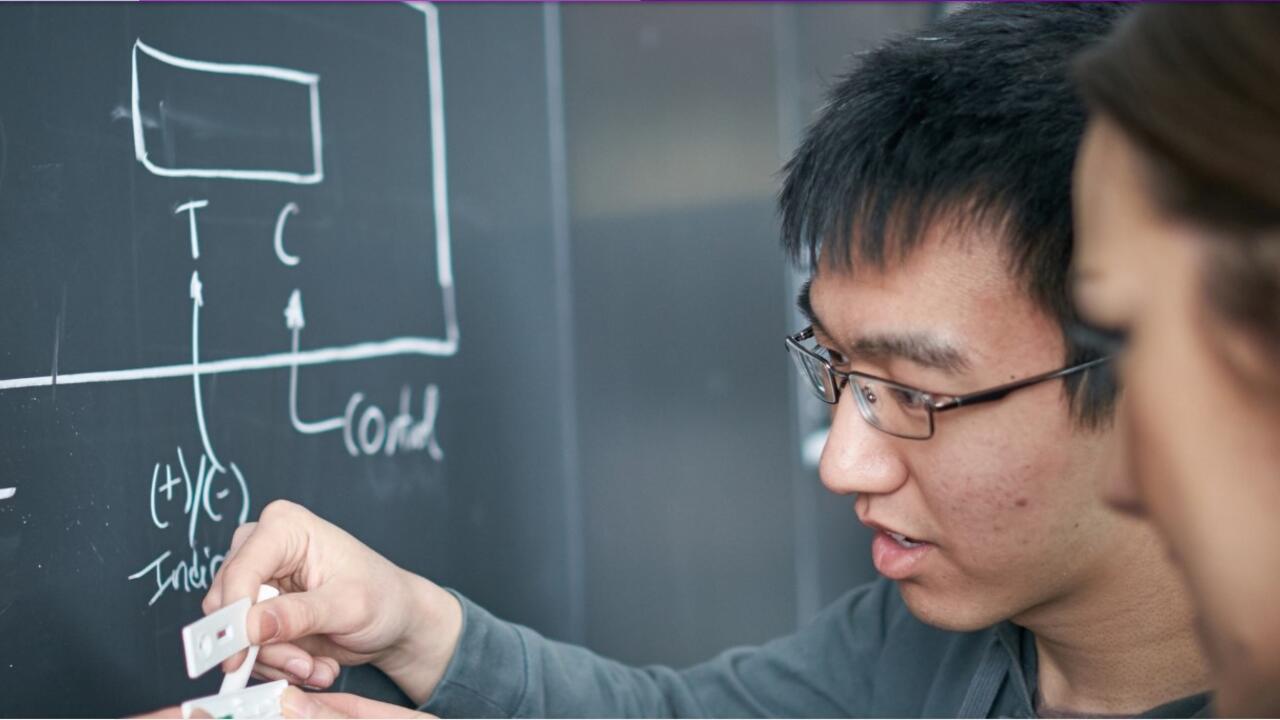 Male student writing on chalkboard with female student observing
