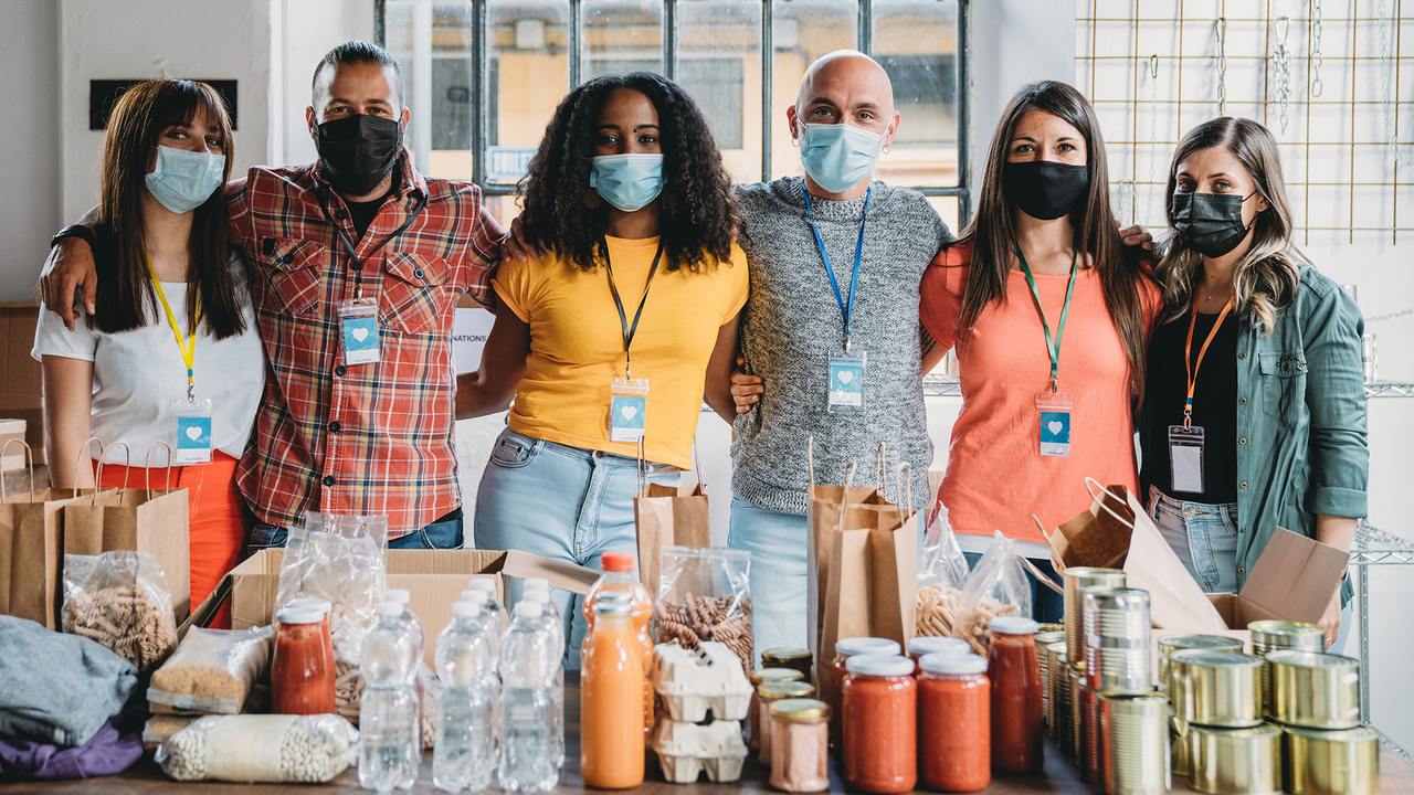 Five diverse young people stand behind a table full of canned goods