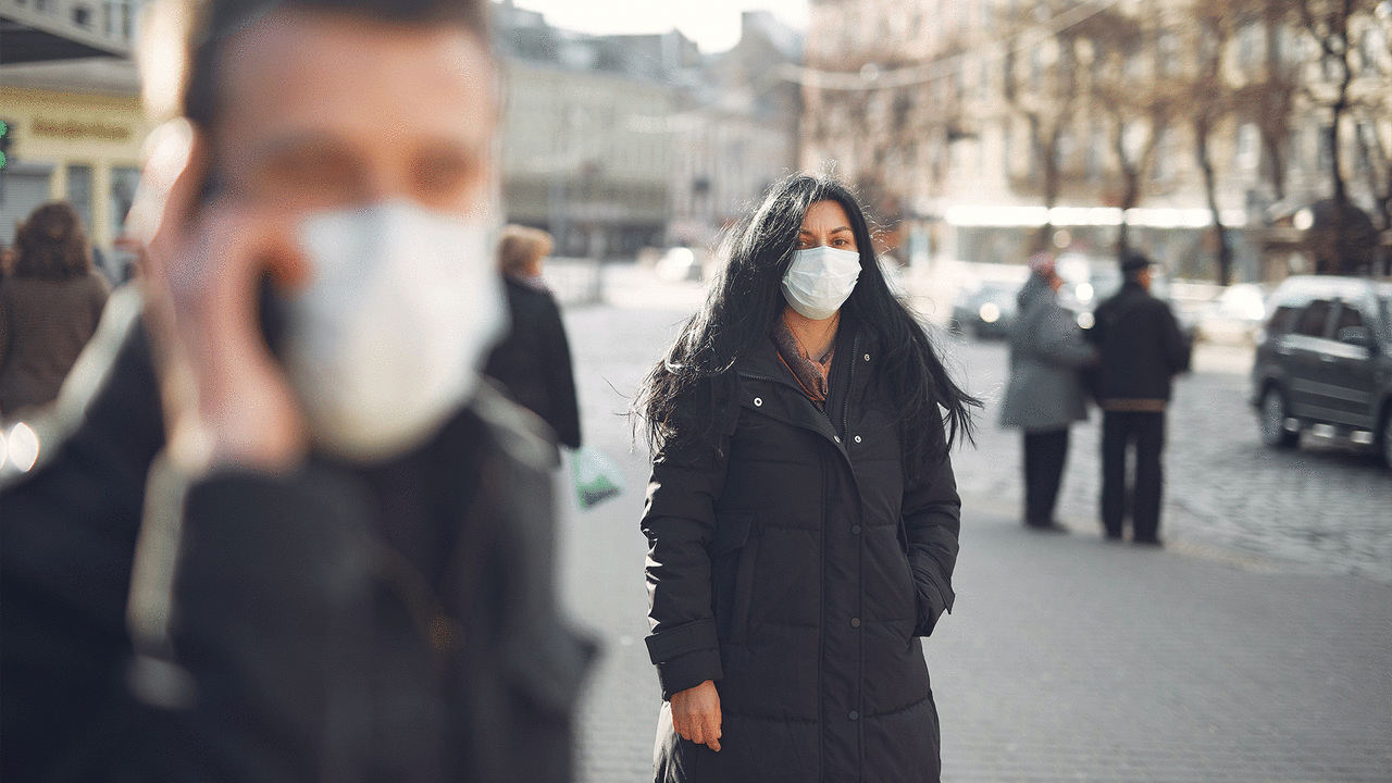 Two people stand wearing masks on a busy street