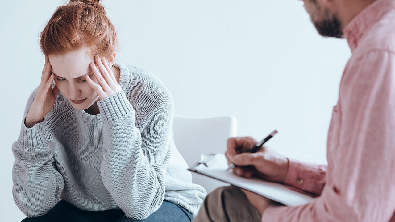 Woman with head in hands as therapist writes notes