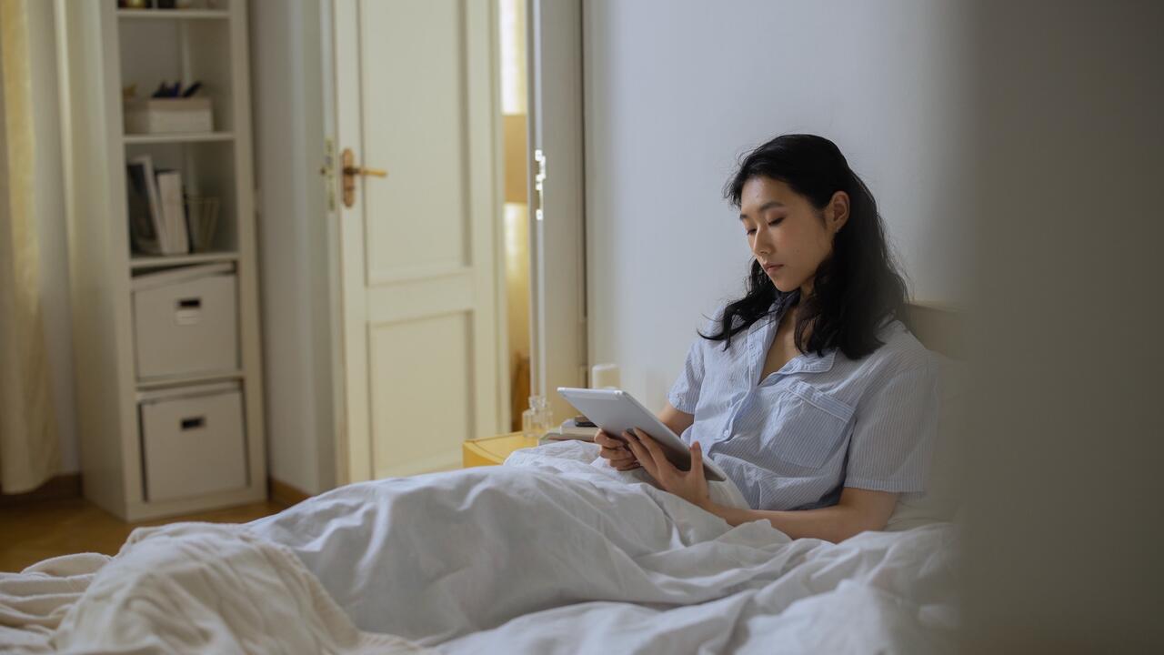 A female lying in bed with a tablet looking at a tablet