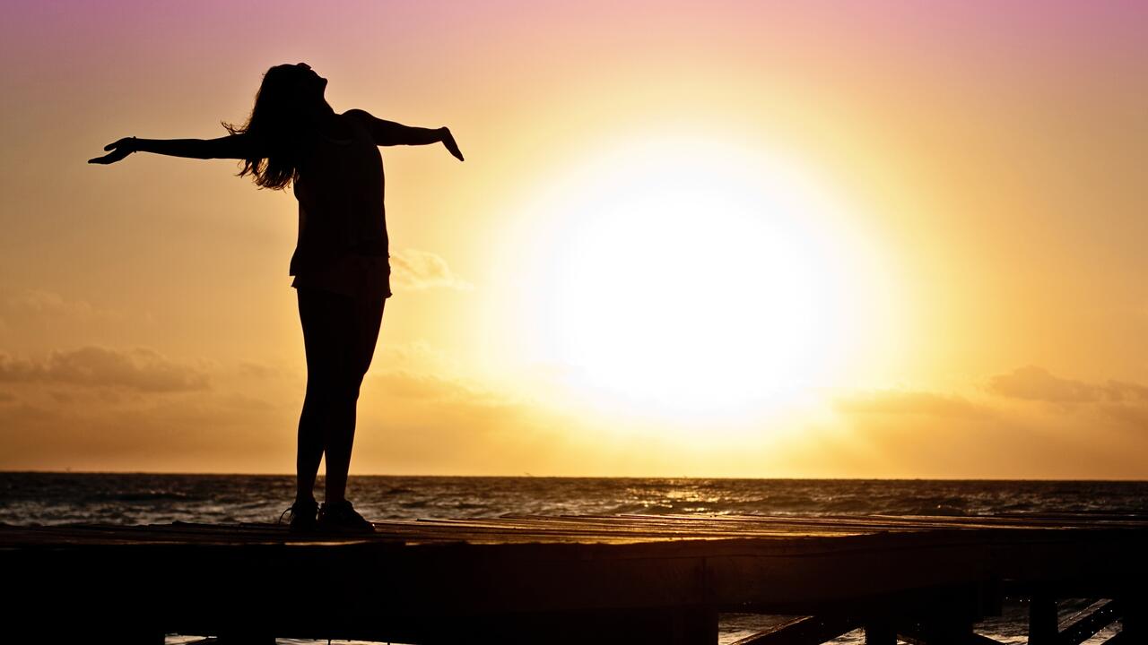 Woman in silhouette standing with her arms outstretched towards the sky.