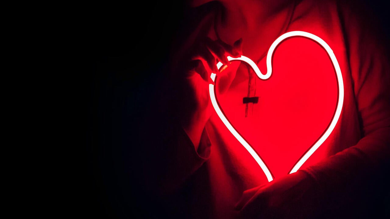 Glowing outline red outline of heart in the dark being held up by two hands