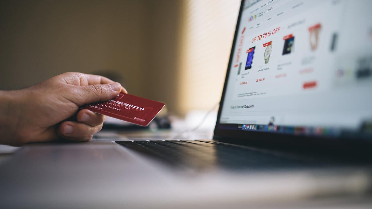 Hand holding credit card in front of laptop