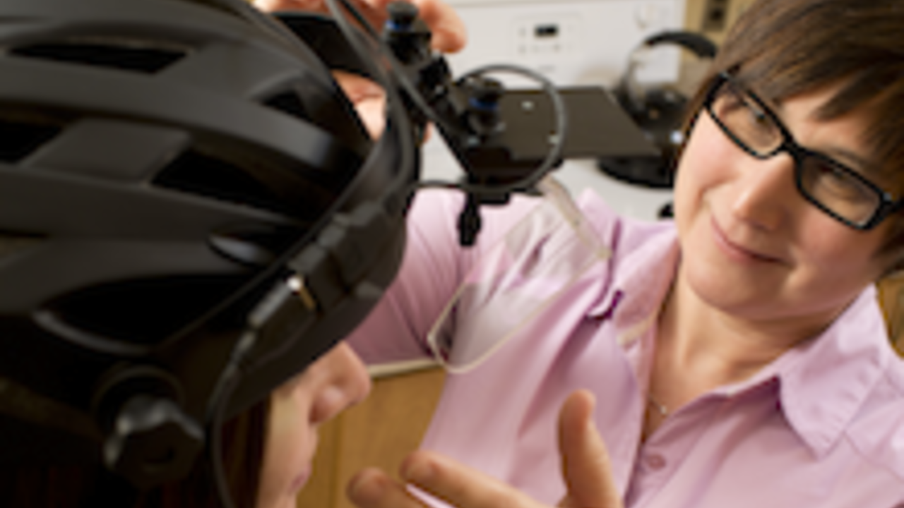Christine Purdon adjusting a camera mounted on a helmet being worn by a young woman.
