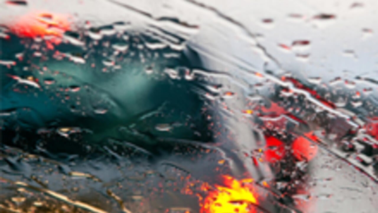 Blurry view through a rain streaked car windshield.