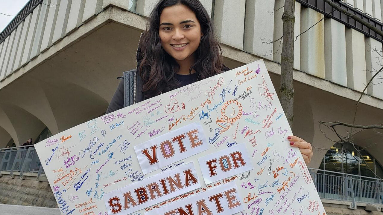 Sabrina holds up a sign covered in signatures that says 