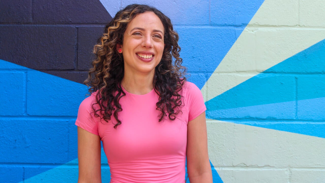 Artist Stephanie Boutari stands in front of a colourful mural and smiles