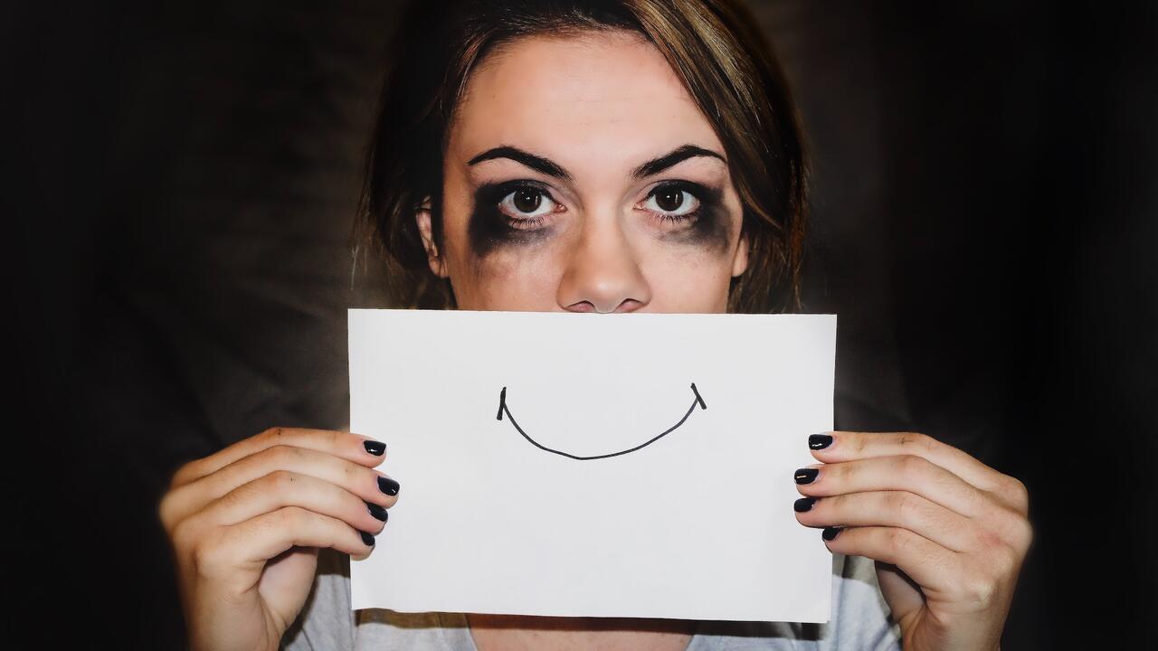 Woman with smudged mascara on her eyes holding a piece of paper with a smile that covers her mouth