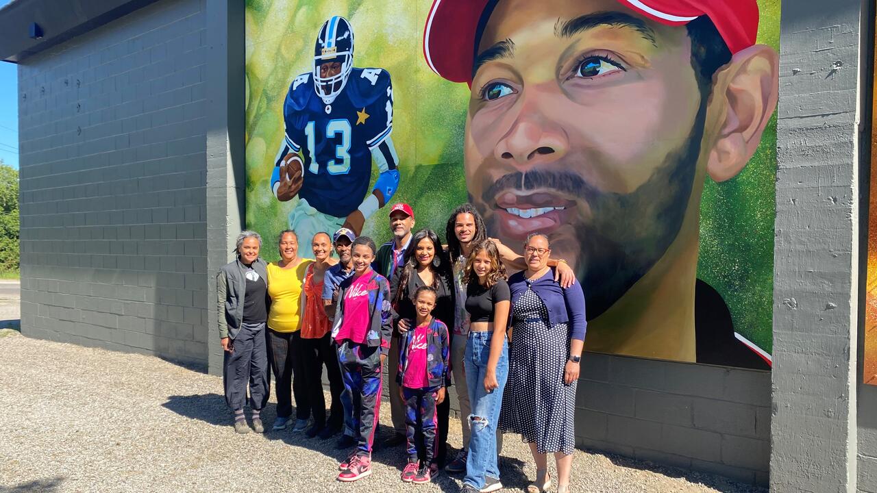 Taly Williams poses with family members in front of a new mural of him on the wall of the arena in Haliburton.