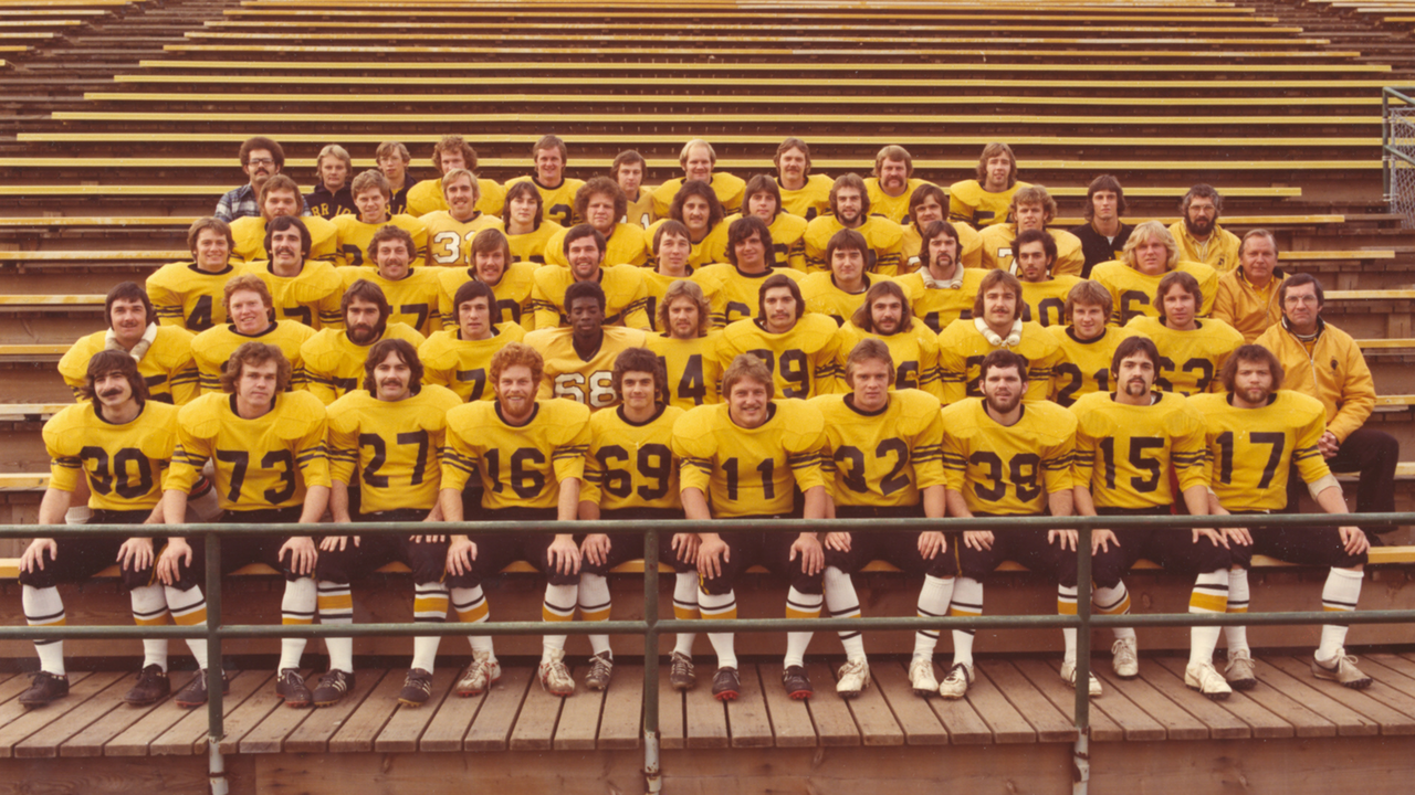 Football players in gold Waterloo jerseys sit on bleachers