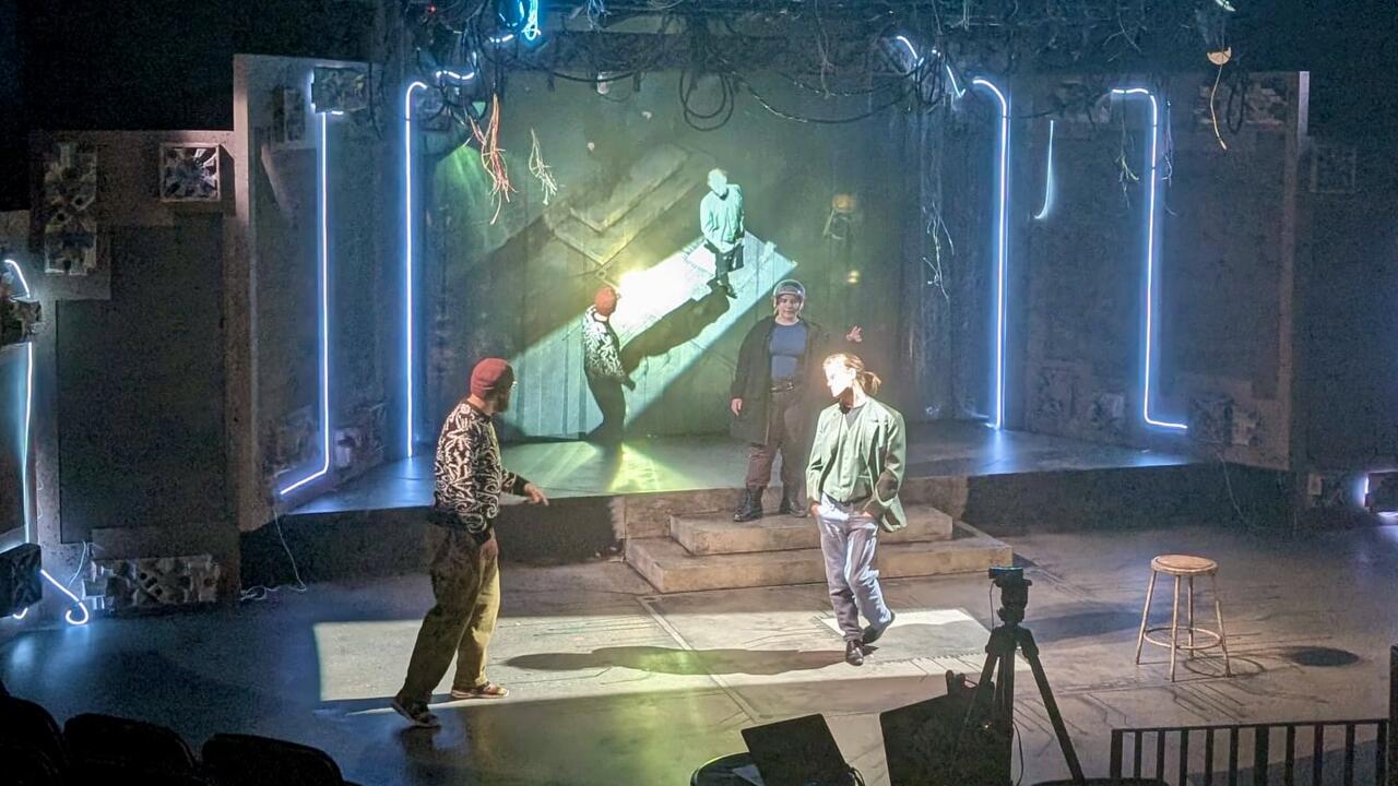 Three people rehearsing on a stage with a VR projection on screen behind them