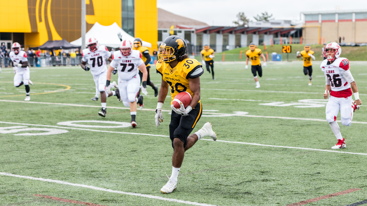 Tyrell Ford runs down a football field pursued by other players