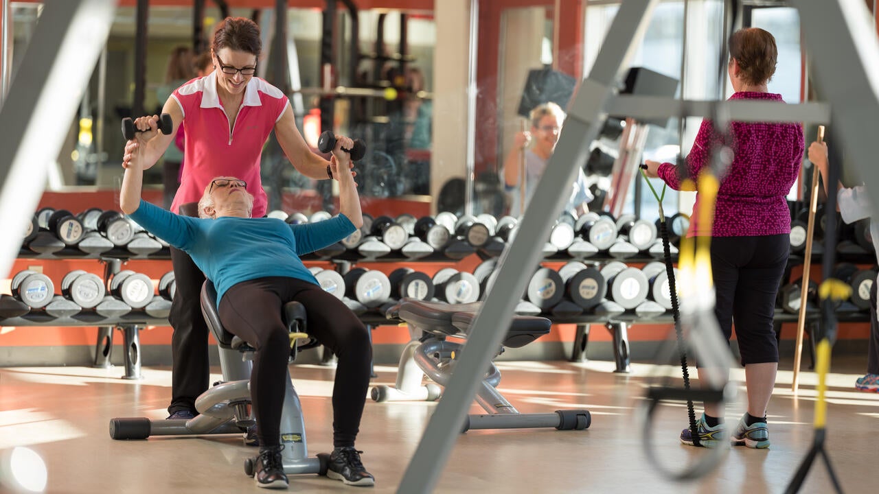 Gym setting with woman on bench press, one assisting, and one to the side