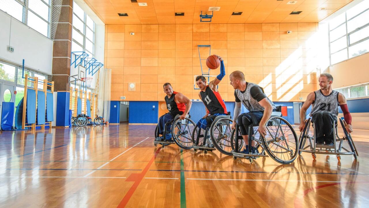 A group of four male athletes play wheelchair basketball on an indoor court.