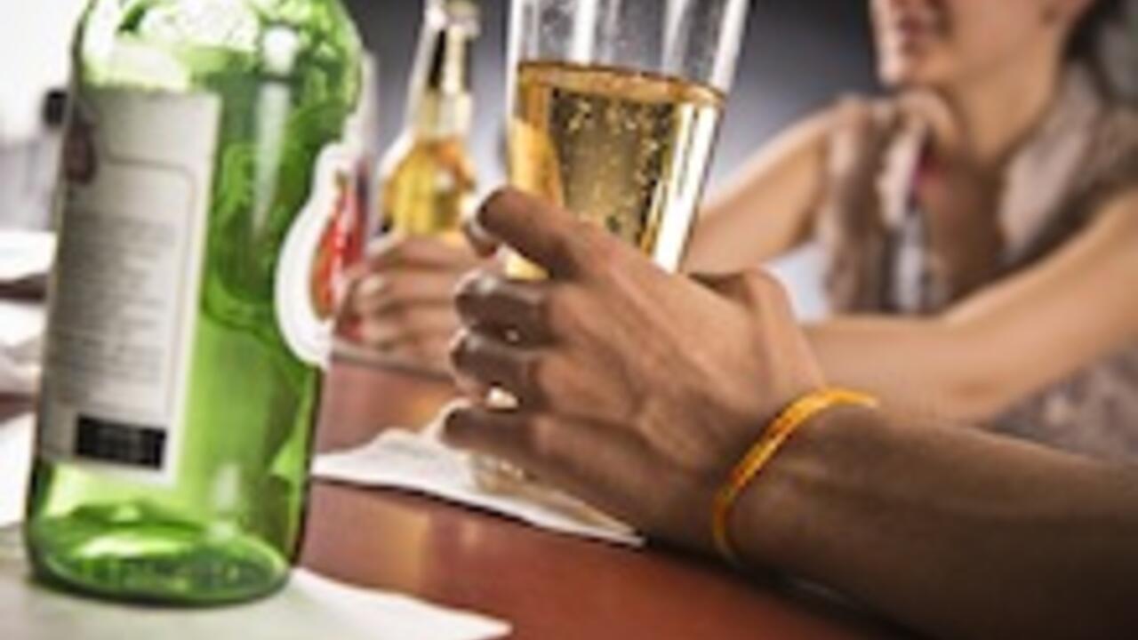 Man's hand holding a glass of beer on a bar.