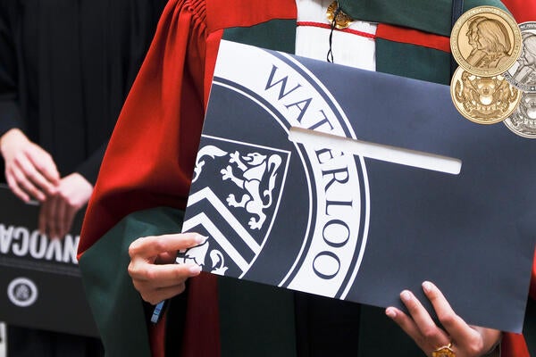 Graduant in PhD regalia holds up diploma folder with Waterloo written on the cover