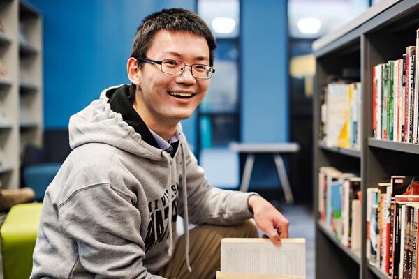 Student holding a book next to library shelf
