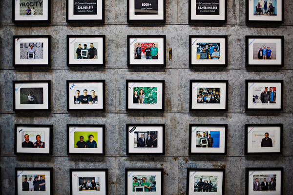 Framed photos of Velocity companies cover a brick wall