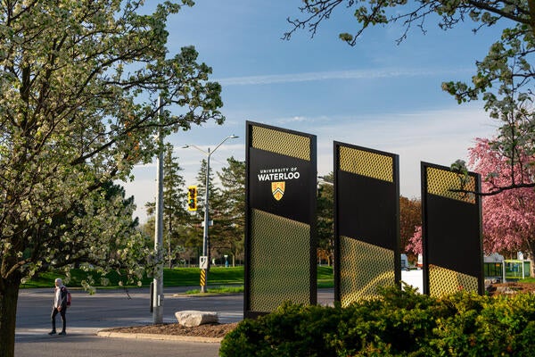 University of Waterloo signage on University Avenue at sunset with a person below the tree walking to cross the street