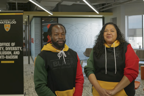 Dr. Christopher Taylor and Jennisha Wilson standing inside the EDI-R office wearing their Black at Waterloo hoodies