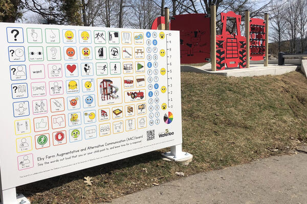 The alternative and augmented communication board near a path and playground structures. Content of the board described in story