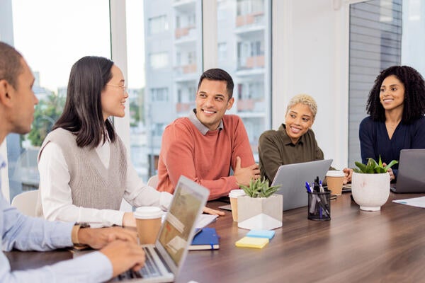 Team sitting around a table having a discussion with their laptops and notes