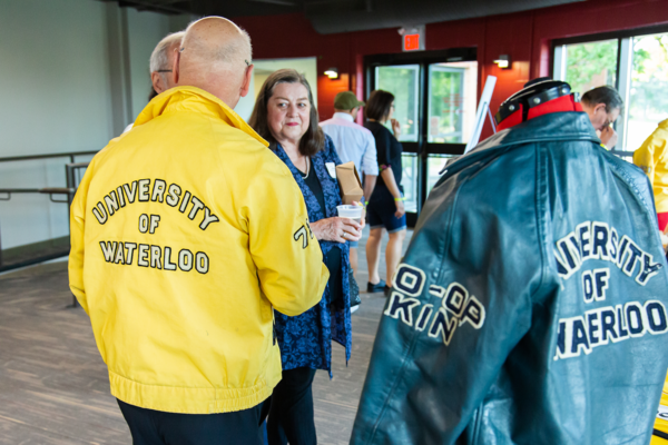 An alum wearing a vintage University of Waterloo jacket, standing beside one on a mannekin