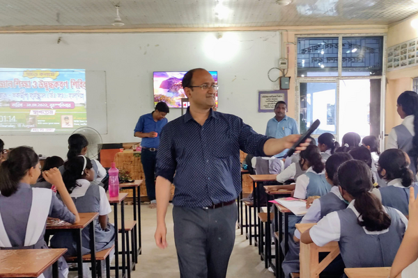 Dr. Rajibul Islam holding a mic addresses students seated at desks in a classroom with a projected presentation at the front.