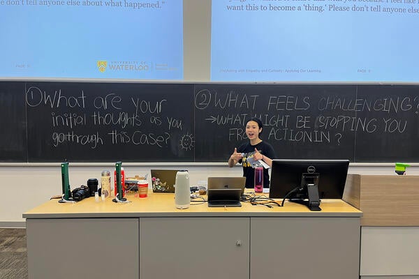 Student in front of a chalkboard smiling with thumbs up