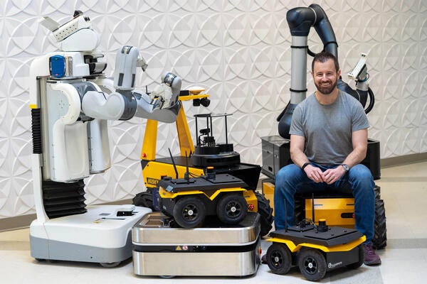 Ryan Gariepy sits among a bunch of Clearpath robots in front of a textured wall