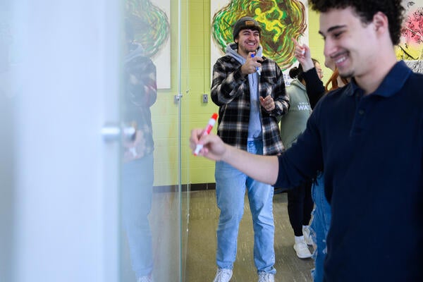 Students at a white board smiling. 