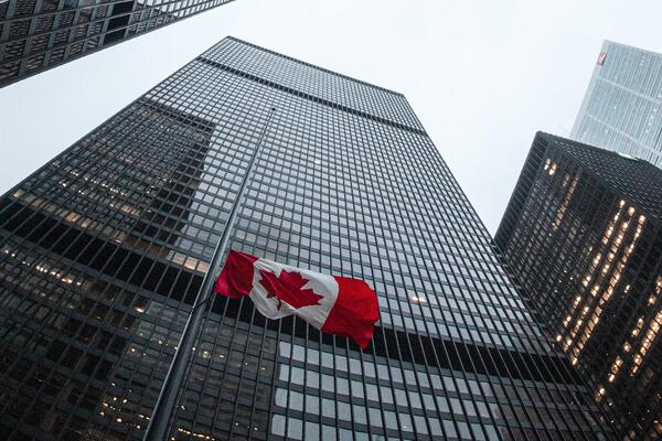 Low angle photo of tall buildings and a Canadian flag at half-mast
