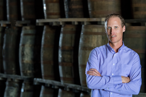 Don Livermore stands, arms crossed, in front of a row of whisky barrels
