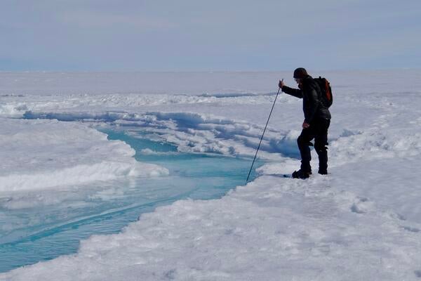 Man inserts a long stick into a stream on top of the ice