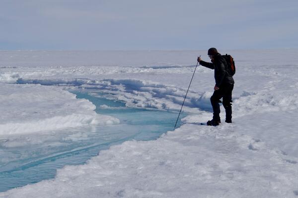 Man inserts measuring stick into a stream on top of ice