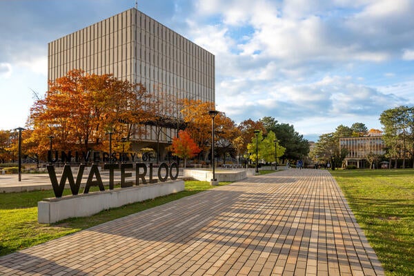 Wide shot of Dana Porter Library in the Fall along with the University of Waterloo sign