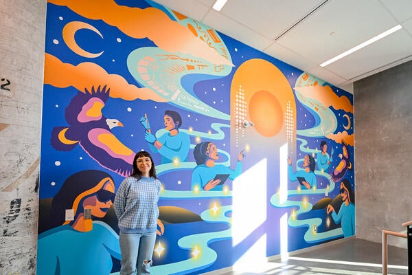 Alanah Jewell standing proudly in front of her Many Hearts, One Mind mural inside the Innovation Arena